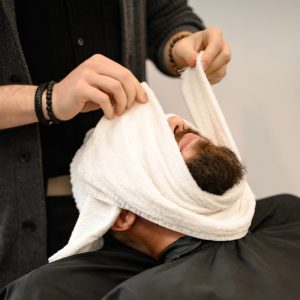 Barbero aplicando una toalla caliente durante el afeitado con navaja en King's Chair Barbershop